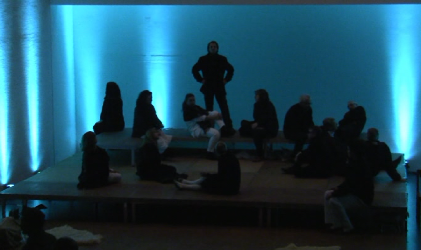Die Bühne in blauem Licht, das Ensemble sitzt und liegt vor einer hell angestrahlten Wand.